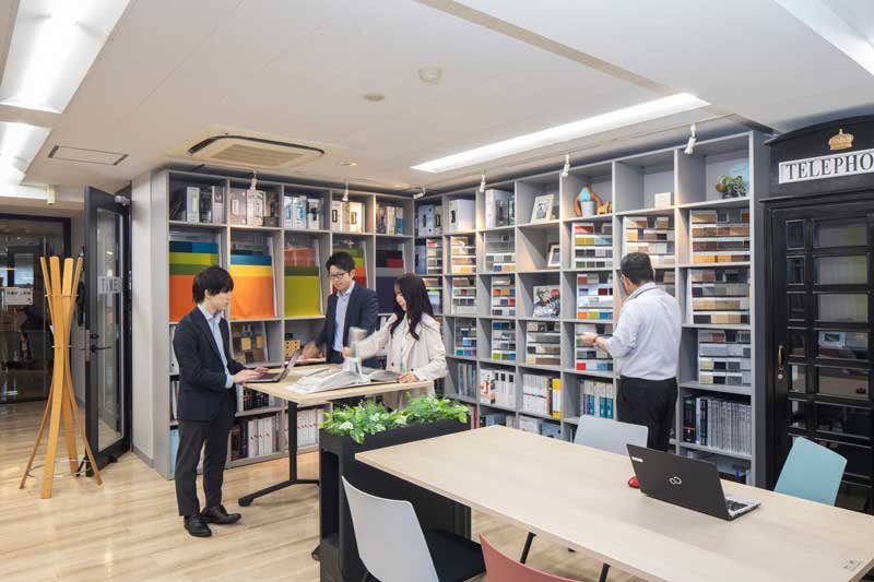 オフィス内の資料コーナー前で社員たちが会話する様子
