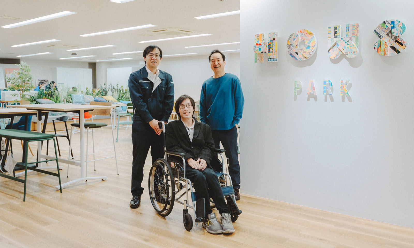 HOWS PARKの入り口の前でインタビューを受けた西林さんと車いすの近藤さんと平畑（ひらはた）さんが笑顔でカメラを見ている様子