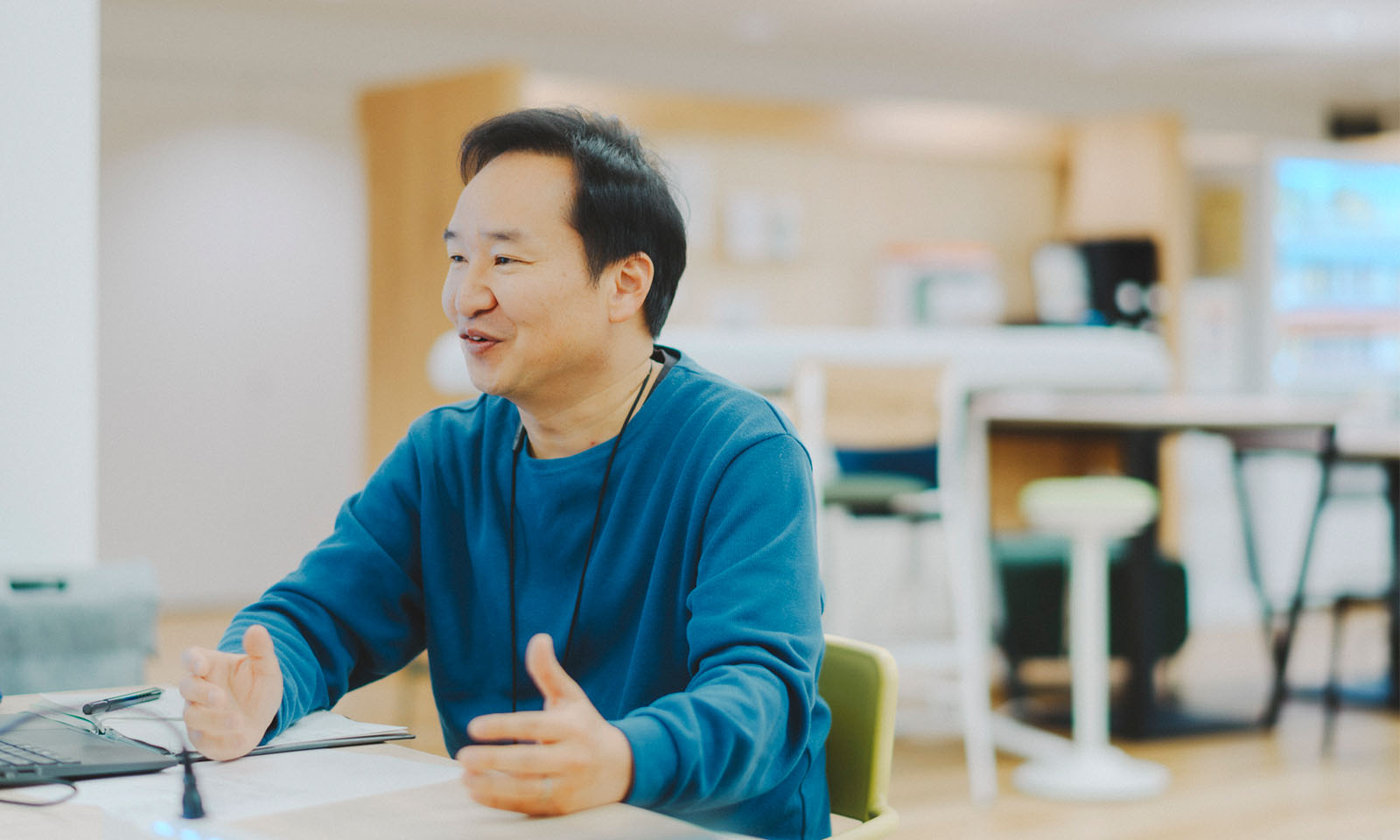 深海の色のような青いセーターを着て、両手を広げながらインタビューに答える西林さん