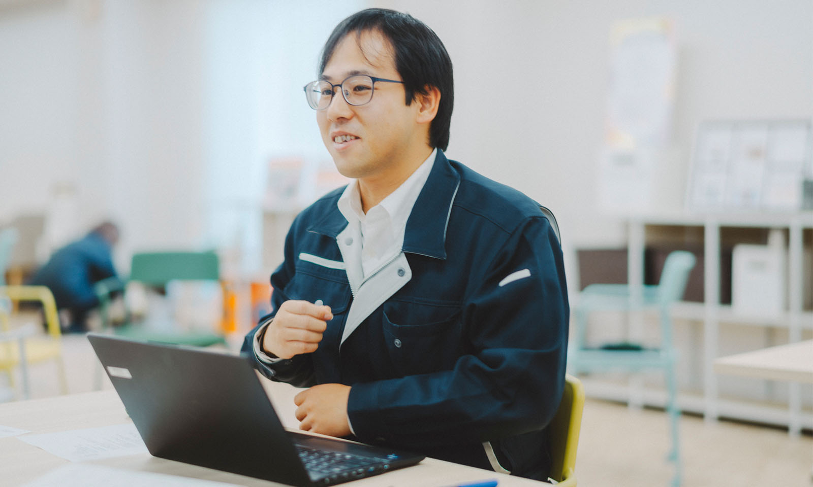 作業着を着て、パソコンを手元に置きながら優しい笑顔でインタビューに答える平畑（ひらはた）さん