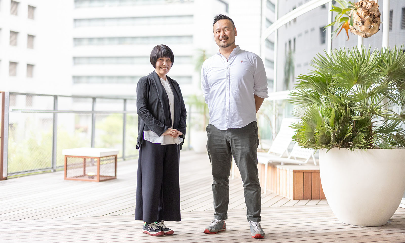 植物のある明るい屋外区間で、栗木さんと武田さんが並んで立っている
