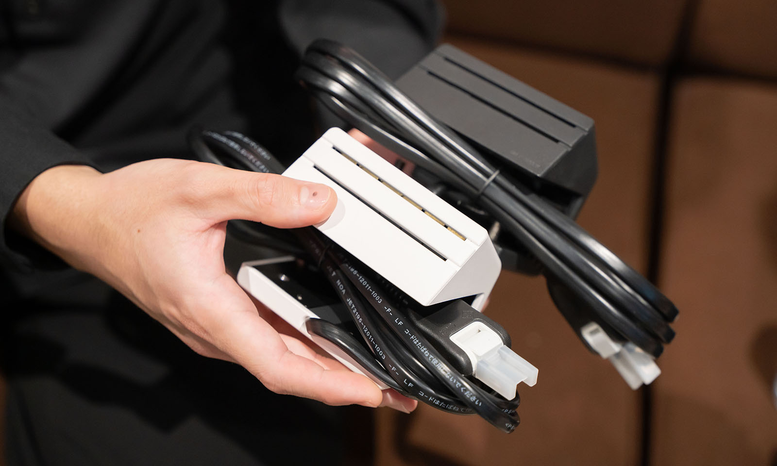 ALTはじまり。白と黒のエナジーラインを持つ手元の写真。真横から見ると家の形をしていて、家の屋根の部分に２つの並んだ直線。そこがコンセントの差し込み口となっており、直線の中のどこに挿してもいいようになっている。また、コンセントのコードは折り畳んで家の形の壁面辺りが窪んでいるため、そのまま挿入ができる。持ち運びがしやすいデザインとなっている。ALTおわり。