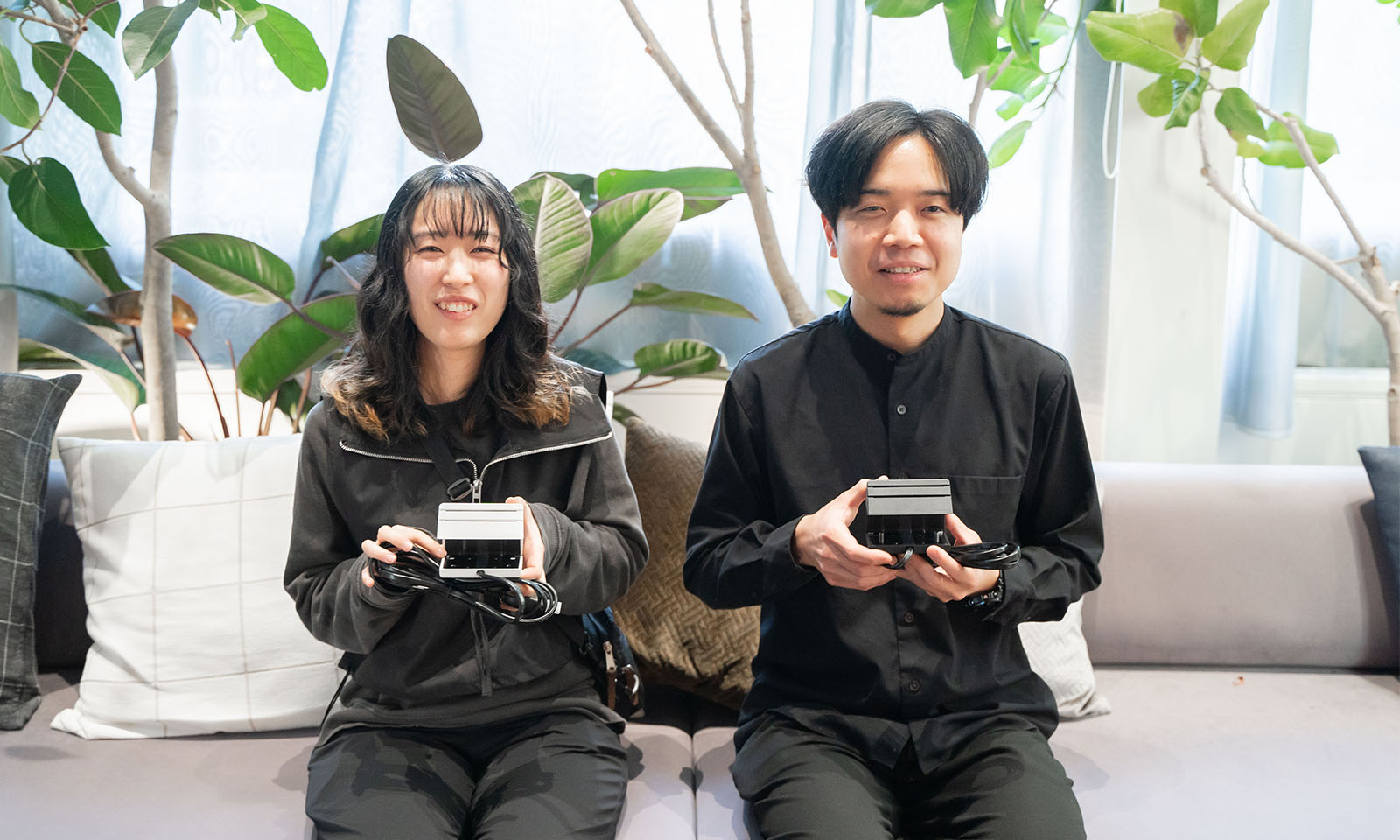 ALTはじまり。観葉植物が後におかれた薄いグレーのソファーに座る２人。ふたりとも優しい笑顔でカメラを見つめる。手元にはそれぞれ白と黒のエナジーラインをもち、その佇まいから思いを込めて作ったのだと伝わる。ALTおわり。