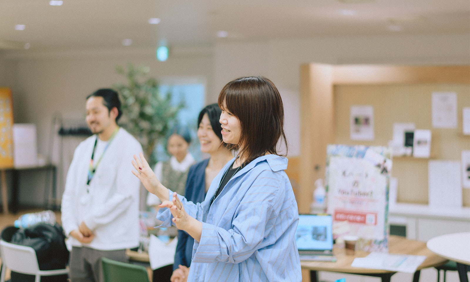 ALTはじまり。オープニングの様子。参加者の目の前に立ち、シャーベットブルーのシャツを着たコクヨの吉村さんが両手を広げて笑顔で説明をしているところ。ALTおわり。