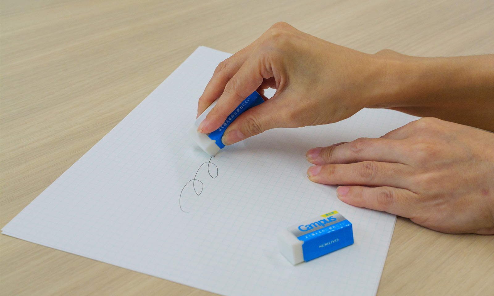 <ALT始まり>インタビュイーの波子さんが、新商品のキャンパス よく消えるのに折れにくい消しゴムを使って、黒線を消している様子<ALT終わり>