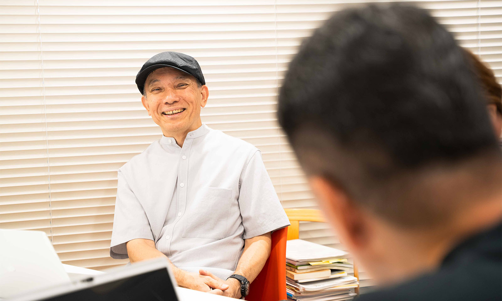 ALTはじまり。薄いグレーの半袖のボタンシャツに、深いグレーのハンチングをかぶり、左腕には黒の時計をつけて微笑む平井教授。研究室にあるオレンジ色の椅子に座り、コクヨの２人にやさしく語りかけている様子。ALTおわり。