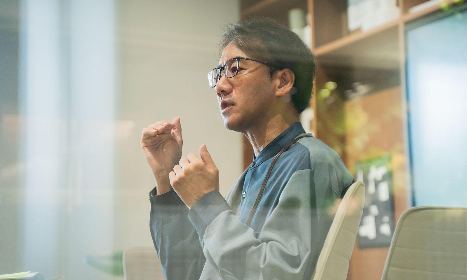 ALTはじまり。両手を使ってジェスチャーをしながら、様々なアイデアを話している丹野さんの横顔。ガラスに反射した植物がうっすらと映り込んでいる。ALTおわり。