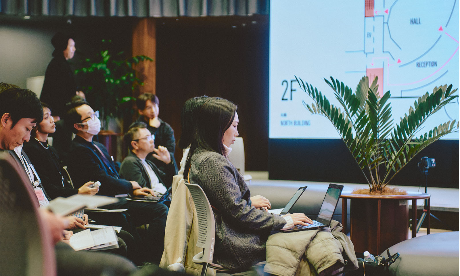 （ALT始まり）登壇者の話を聞く参加者の人々。性別や年齢や服装は様々。手元のノートやパソコンでメモをとっている人もいる。（ALT終わり）