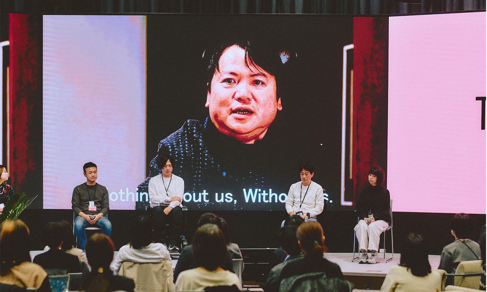 （ALT始まり）くまがいしんいちろう教授からのビデオメッセージがスクリーンに投影されている様子。画面下には英語で字幕が表示されている。（ALT終わり）