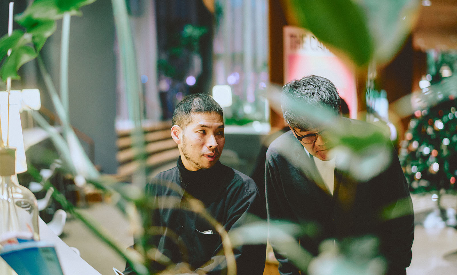 （ALT始まり）リードユーザーの男性、ひがしのさんの声に、グループメンバーの男性が体を寄せて耳を傾けている様子。（ALT終わり）