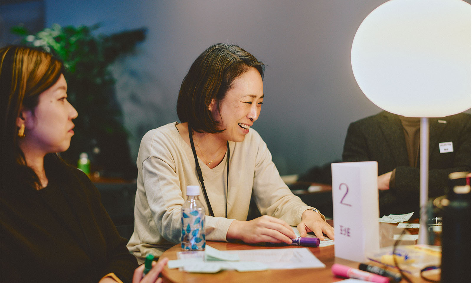 （ALT始まり）グループごとに着座し、気づきや疑問について話し合う参加者たちの様子。女性が笑顔で話す姿が写っている。（ALT終わり）