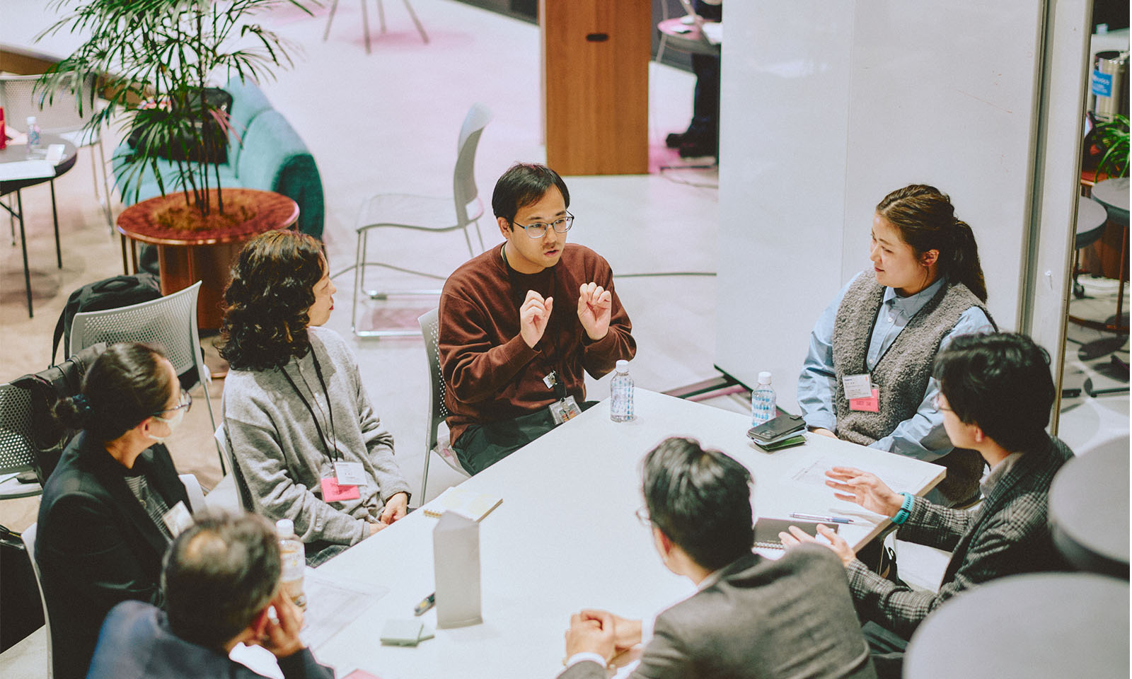 （ALT始まり）グループで着座して気づきを共有する参加者たち。7名がひとつのテーブルを囲んで話し合っている様子。（ALT終わり）