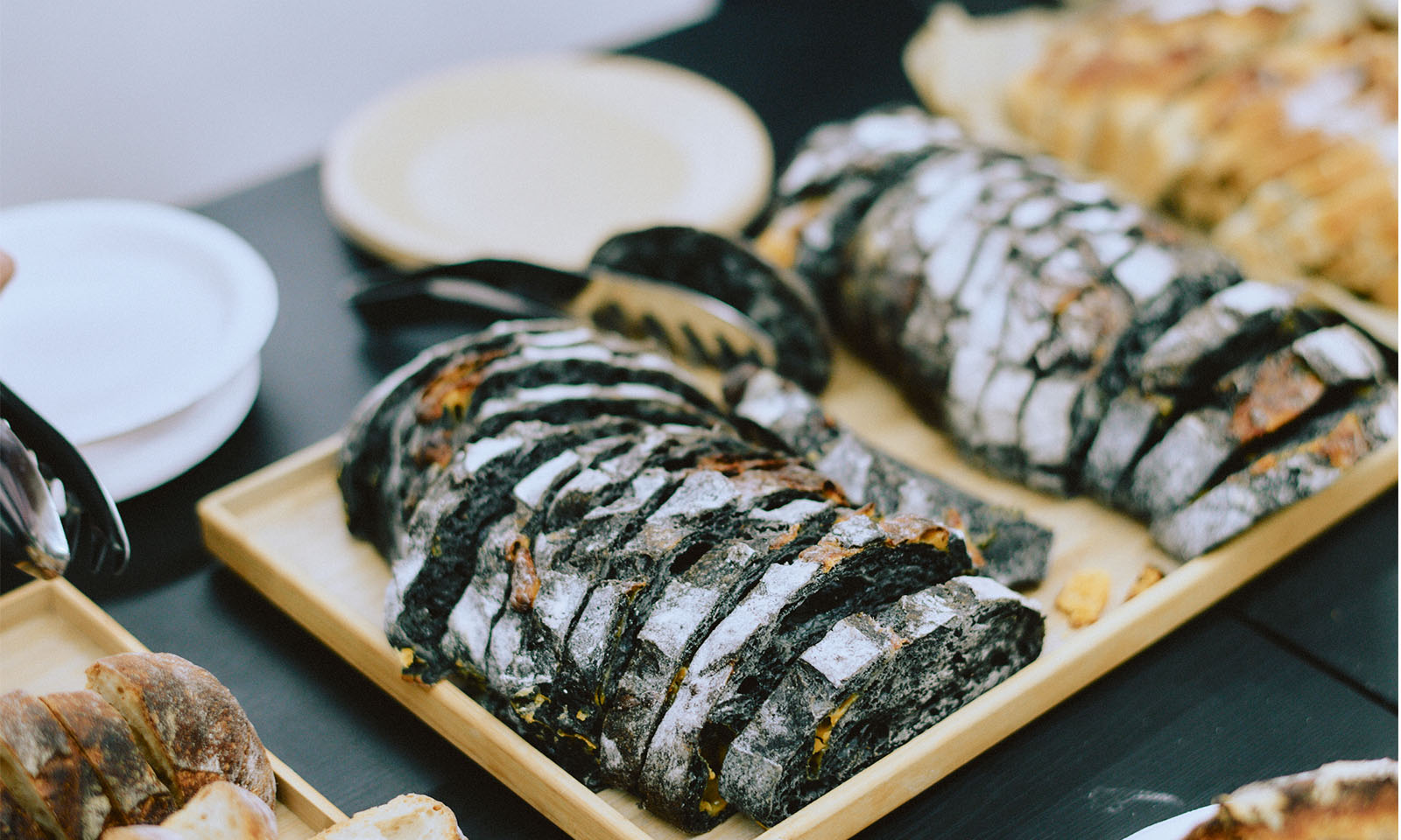 （ALT始まり）ケータリングで用意されていたパン。色々な種類のパンがスライスされて木製のトレーに並べられている。（ALT終わり）