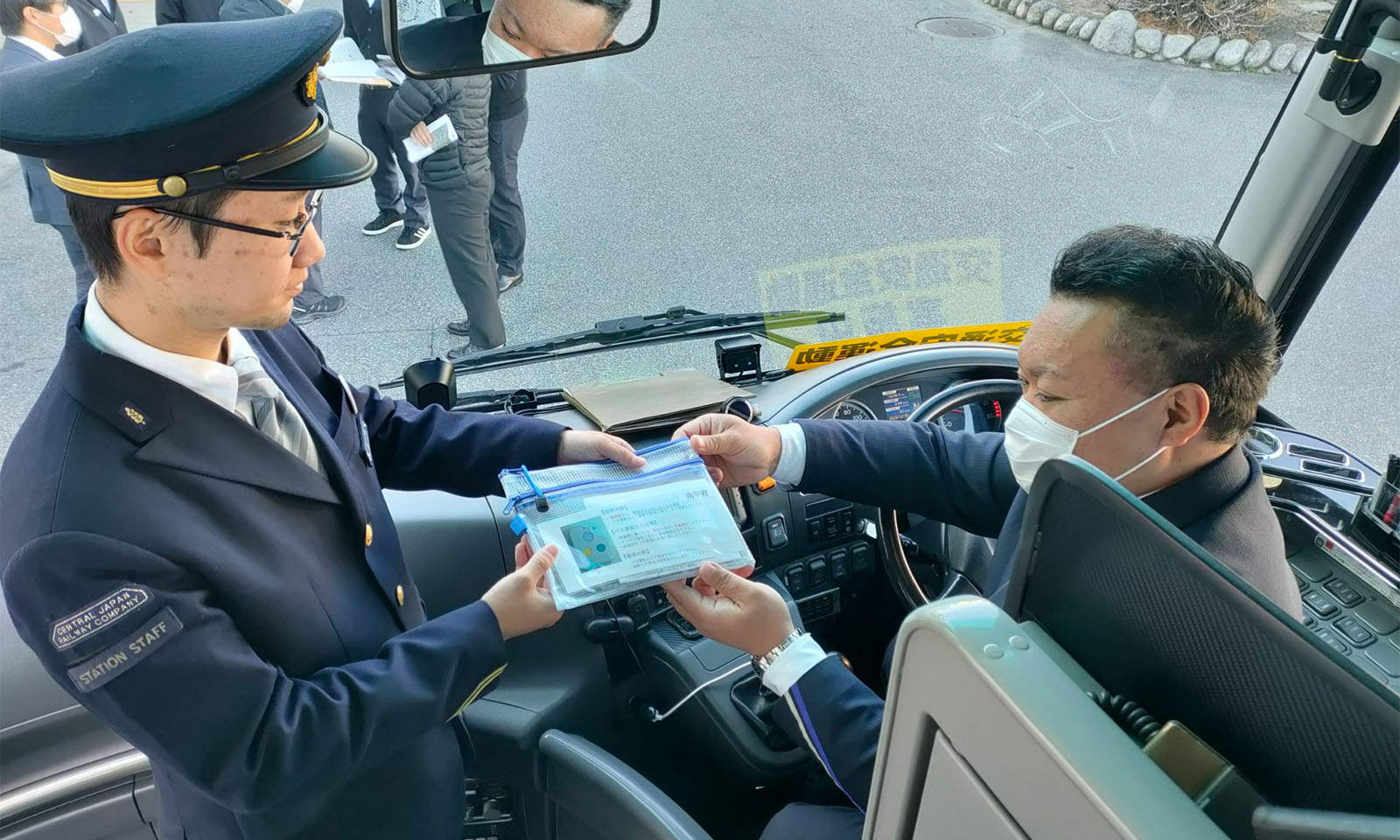 （ALT始まり）バス車内にて、実際にはろここトークの端末が入ったケースをバス運転士へ手渡す様子。（ALT終わり）