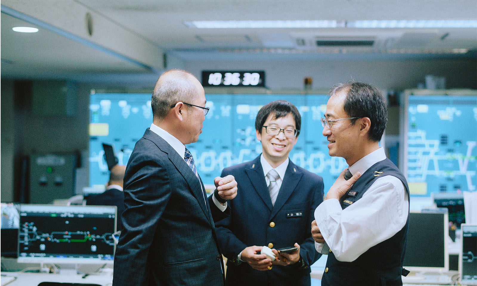 （ALT始まり）談笑する3名。背景には運行状況などが可視化されている。（ALT終わり）