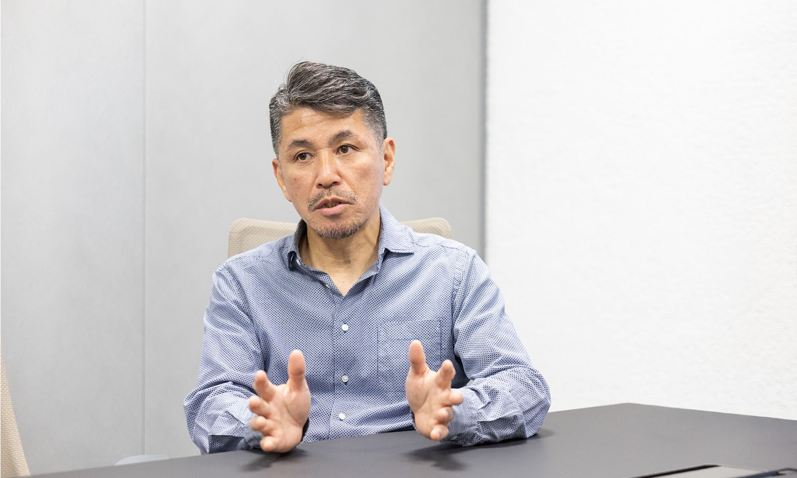 ALTはじまり。テーブルの前に座って手を広げて説明している。ALTおわり。