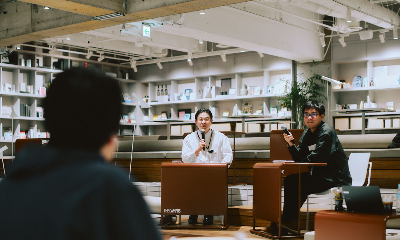 ALTはじまり。イベントの様子の一部。登壇者が参加者の質問に笑顔で応えている。登壇者の後ろには壁一面に埋め込まれている白い棚があり、天井はやや高めで、全体的に白と木目調の家具で揃えられ、清潔感とナチュラルさのある色味が印象的な空間になっている。ALTおわり。