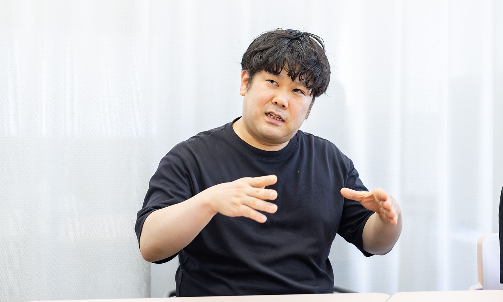 ALTはじまり。画像：インタビュー中、説明する小松原さん。黒いTシャツを着た男性。画像おわり。ALTおわり。