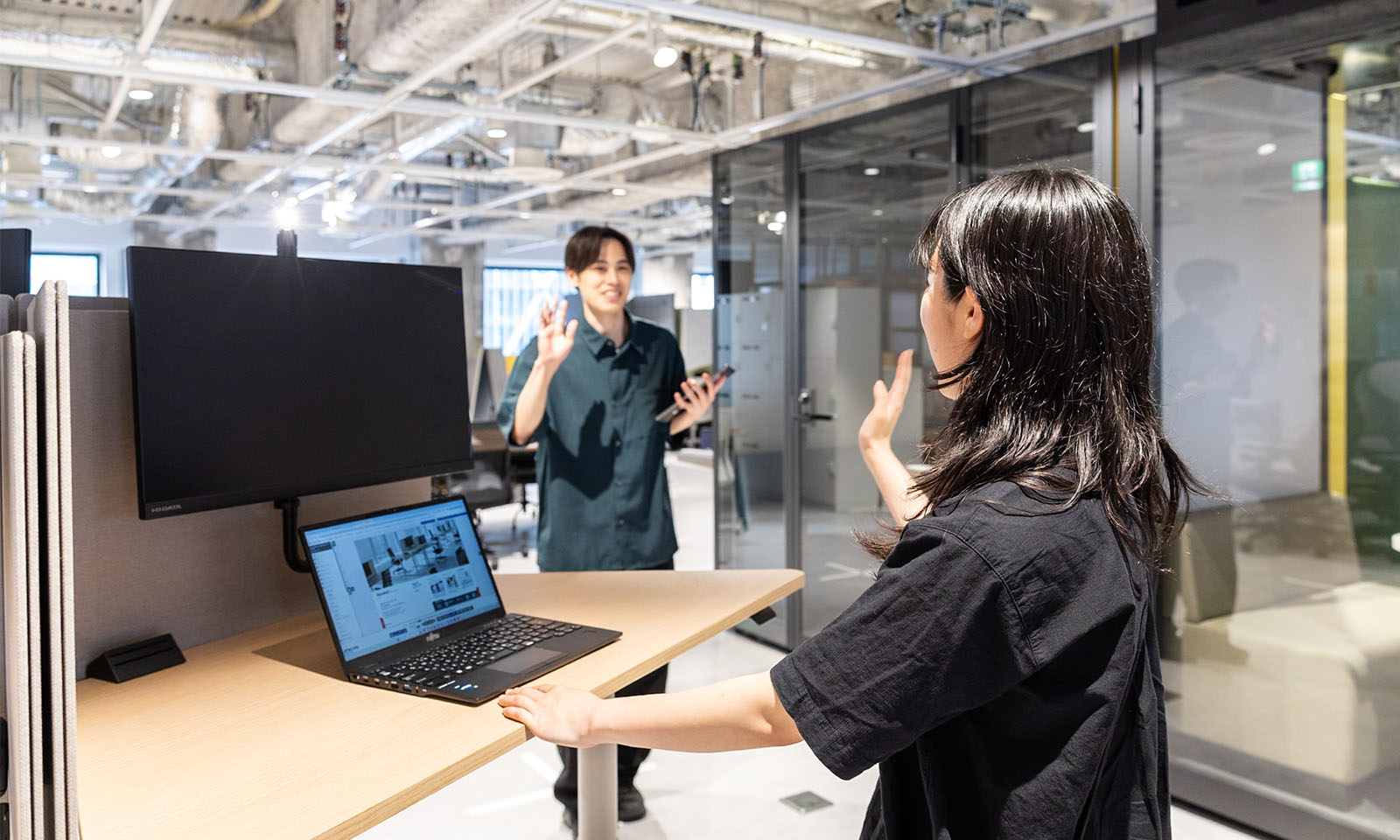 ALTはじまり。画像：台形の昇降テーブルで作業している人に向かって、話しかけるために別の人近づいてきている様子の再現。画像おわり。ALTおわり。