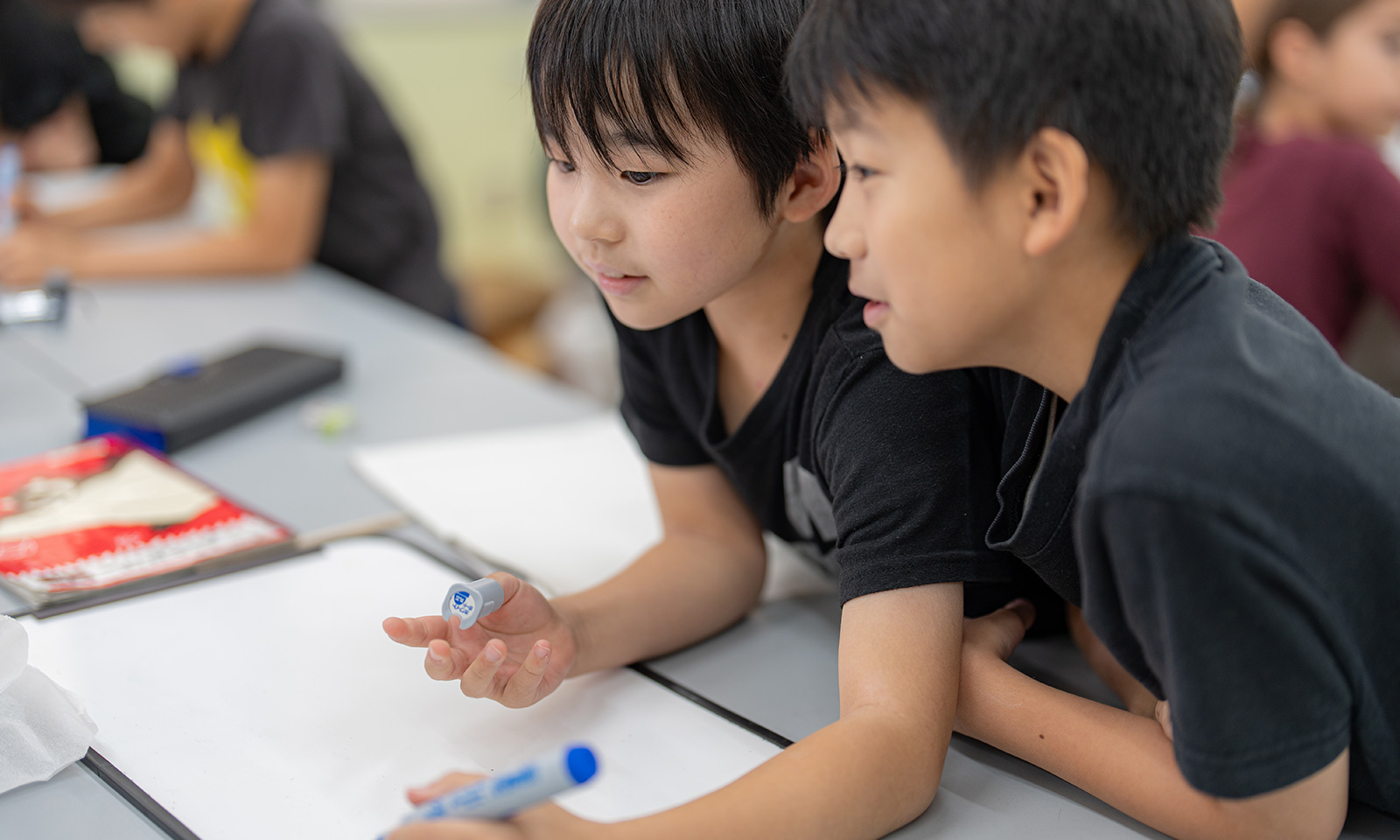 2人の黒い服を着た男の子が、手元のホワイトボードにペンでアイデアを書いている様子